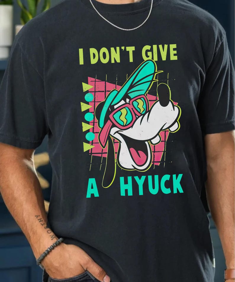 Retro 90s-style Disney shirt featuring Goofy wearing neon sunglasses and a sideways cap with bold text that says "I Don't Give A Hyuck." Colorful geometric background with a distressed vintage look. Perfect for fans of A Goofy Movie, Disney humor shirts, family vacations, or retro-themed Disney park outfits.