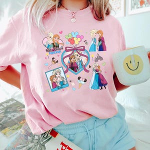 Cute coquette-style Disney Frozen shirt featuring Elsa and Anna with hearts, bows, and pastel icons, ideal for sisters and best friends.
