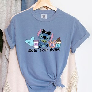 Stitch Best Day Ever Shirt featuring Stitch hugging Baby Yoda, surrounded by colorful Disney snacks like Mickey-shaped donuts, cotton candy, ice cream, and a Disney coffee cup. Cute and fun design perfect for a Disney Snacks Sweatshirt or T-shirt, great for Disney park trips, foodie gifts, and Stitch fans.