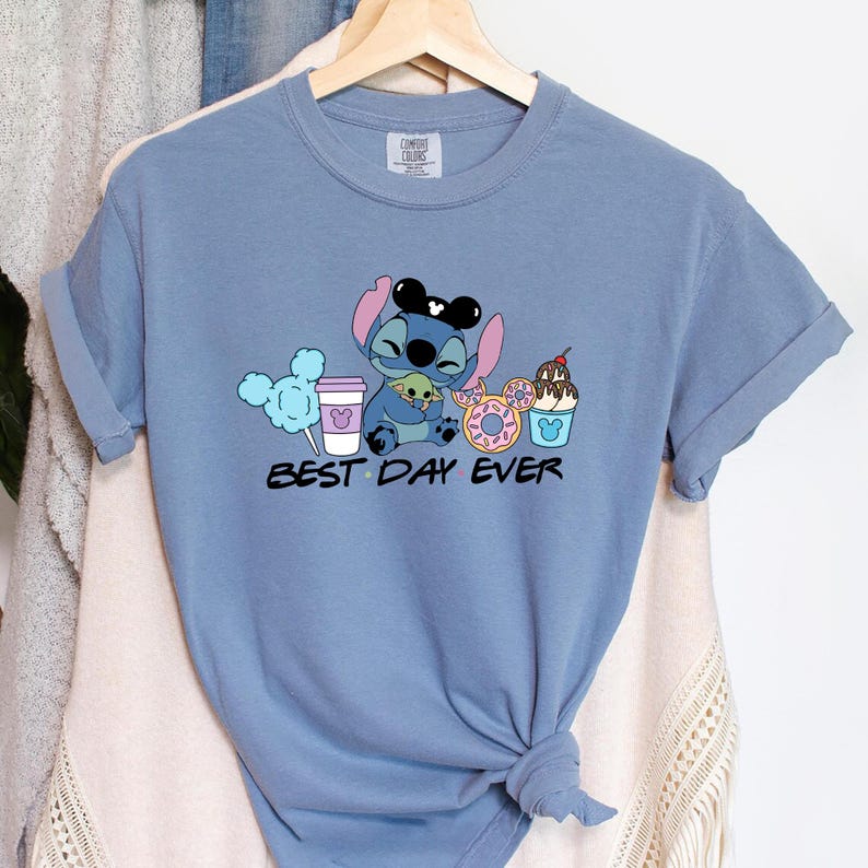 Stitch Best Day Ever Shirt featuring Stitch hugging Baby Yoda, surrounded by colorful Disney snacks like Mickey-shaped donuts, cotton candy, ice cream, and a Disney coffee cup. Cute and fun design perfect for a Disney Snacks Sweatshirt or T-shirt, great for Disney park trips, foodie gifts, and Stitch fans.