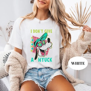 Retro 90s-style Disney shirt featuring Goofy wearing neon sunglasses and a sideways cap with bold text that says "I Don't Give A Hyuck." Colorful geometric background with a distressed vintage look. Perfect for fans of A Goofy Movie, Disney humor shirts, family vacations, or retro-themed Disney park outfits.