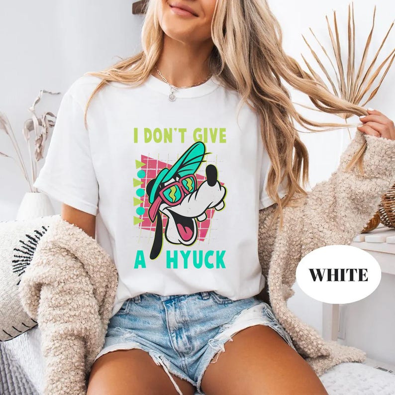Retro 90s-style Disney shirt featuring Goofy wearing neon sunglasses and a sideways cap with bold text that says "I Don't Give A Hyuck." Colorful geometric background with a distressed vintage look. Perfect for fans of A Goofy Movie, Disney humor shirts, family vacations, or retro-themed Disney park outfits.