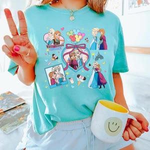 Cute coquette-style Disney Frozen shirt featuring Elsa and Anna with hearts, bows, and pastel icons, ideal for sisters and best friends.