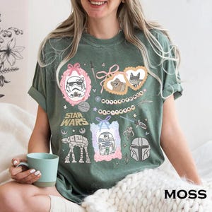 Retro pastel water color coquette Star Wars shirt with kawaii-style Stormtrooper, R2D2, AT-AT, Ewok, and Mandalorian helmet in watercolor frames with bows and hearts, perfect for Disney trip or Star Wars Day outfit.