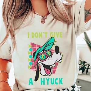 Retro 90s-style Disney shirt featuring Goofy wearing neon sunglasses and a sideways cap with bold text that says "I Don't Give A Hyuck." Colorful geometric background with a distressed vintage look. Perfect for fans of A Goofy Movie, Disney humor shirts, family vacations, or retro-themed Disney park outfits.