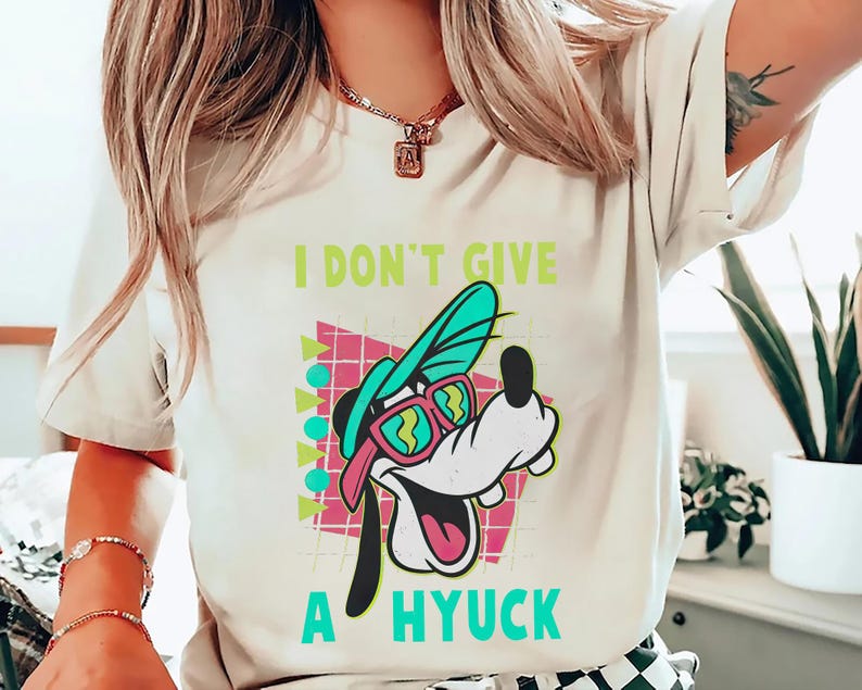 Retro 90s-style Disney shirt featuring Goofy wearing neon sunglasses and a sideways cap with bold text that says "I Don't Give A Hyuck." Colorful geometric background with a distressed vintage look. Perfect for fans of A Goofy Movie, Disney humor shirts, family vacations, or retro-themed Disney park outfits.