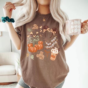 retro disney halloween shirt design featuring coquette bow mickey ears pumpkins fall leaves cozy autumn coffee cup tis the season beaded necklace and cute disney fall vibes illustration
