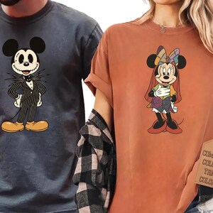 May include: Two t-shirts featuring cartoon characters. One is a dark gray shirt with Jack Skellington from The Nightmare Before Christmas. The other is a burnt orange shirt with Minnie Mouse in a Halloween costume. Both shirts have a tag that says "Comfort Colors".