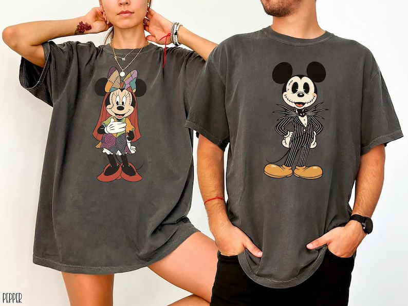 May include: Two dark gray t-shirts featuring Disney characters. One shirt displays Minnie Mouse in a colorful patchwork outfit, and the other showcases Jack Skellington from The Nightmare Before Christmas. Both shirts have short sleeves.