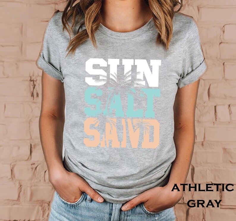 Bold beach-themed graphic with the words 'Sun Salt Sand' in large block letters, featuring palm trees and coastal colors—perfect for summer vacation or beach day t-shirts.