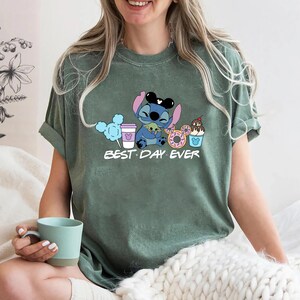 Stitch Best Day Ever Shirt featuring Stitch hugging Baby Yoda, surrounded by colorful Disney snacks like Mickey-shaped donuts, cotton candy, ice cream, and a Disney coffee cup. Cute and fun design perfect for a Disney Snacks Sweatshirt or T-shirt, great for Disney park trips, foodie gifts, and Stitch fans.