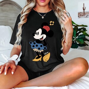 May include: Black t-shirt featuring a graphic of Minnie Mouse wearing a blue polka dot skirt with the word "Disney" printed on the bottom.
