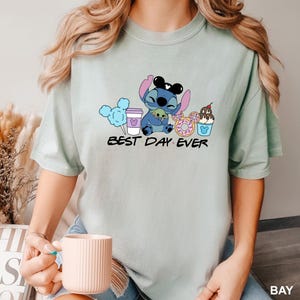 Stitch Best Day Ever Shirt featuring Stitch hugging Baby Yoda, surrounded by colorful Disney snacks like Mickey-shaped donuts, cotton candy, ice cream, and a Disney coffee cup. Cute and fun design perfect for a Disney Snacks Sweatshirt or T-shirt, great for Disney park trips, foodie gifts, and Stitch fans.