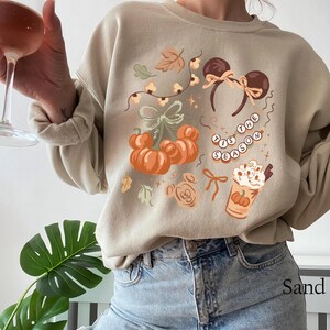 retro disney halloween shirt design featuring coquette bow mickey ears pumpkins fall leaves cozy autumn coffee cup tis the season beaded necklace and cute disney fall vibes illustration