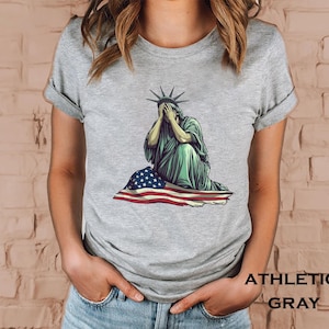 Emotional graphic of the Statue of Liberty sitting with her face in her hands wrapped in a tattered American flag symbolizing sorrow or concern for the nation perfect for political statement shirts freedom of speech tees protest art apparel or USA patriotism designs that express American values or disappointment in the state of the country