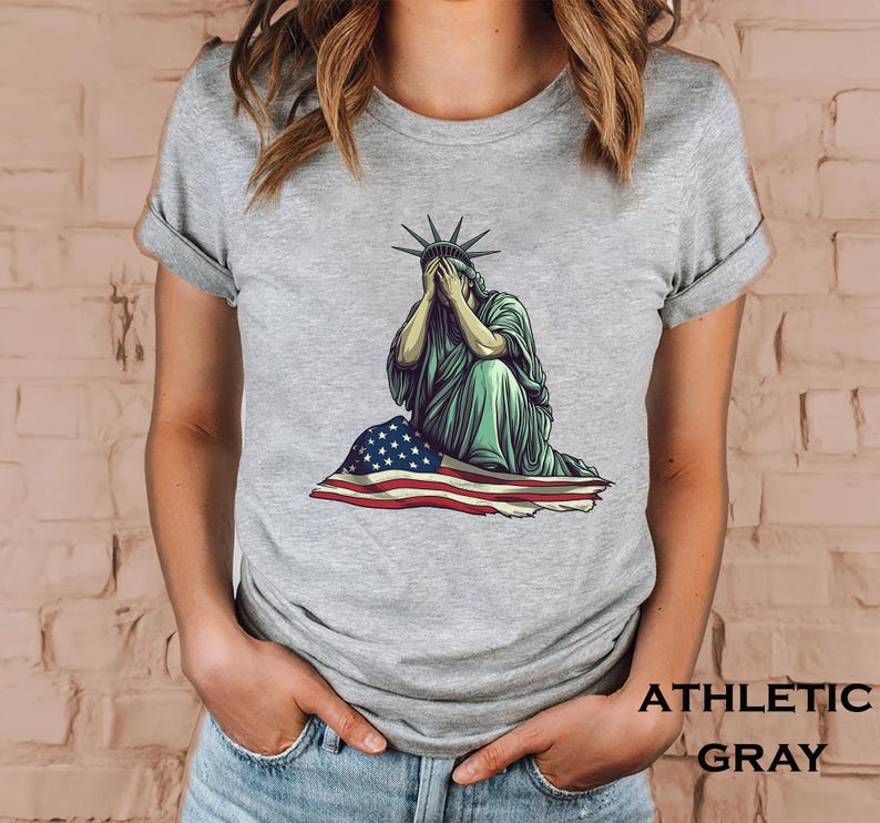 Emotional graphic of the Statue of Liberty sitting with her face in her hands wrapped in a tattered American flag symbolizing sorrow or concern for the nation perfect for political statement shirts freedom of speech tees protest art apparel or USA patriotism designs that express American values or disappointment in the state of the country