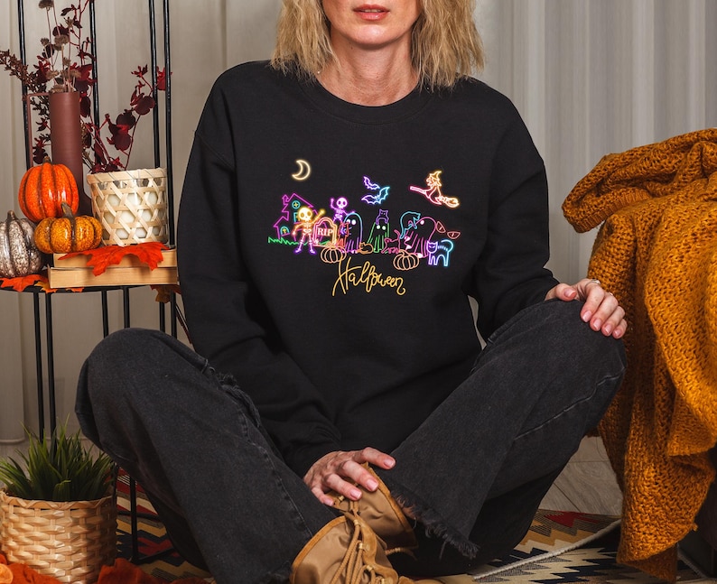 Glow-in-the-dark Halloween graphic tee showcasing neon spooky skeletons, playful ghosts, and a witch, ideal for Halloween events and trick-or-treating.