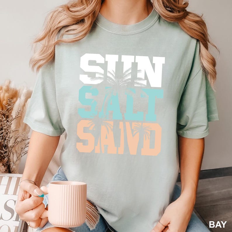 Bold beach-themed graphic with the words 'Sun Salt Sand' in large block letters, featuring palm trees and coastal colors—perfect for summer vacation or beach day t-shirts.