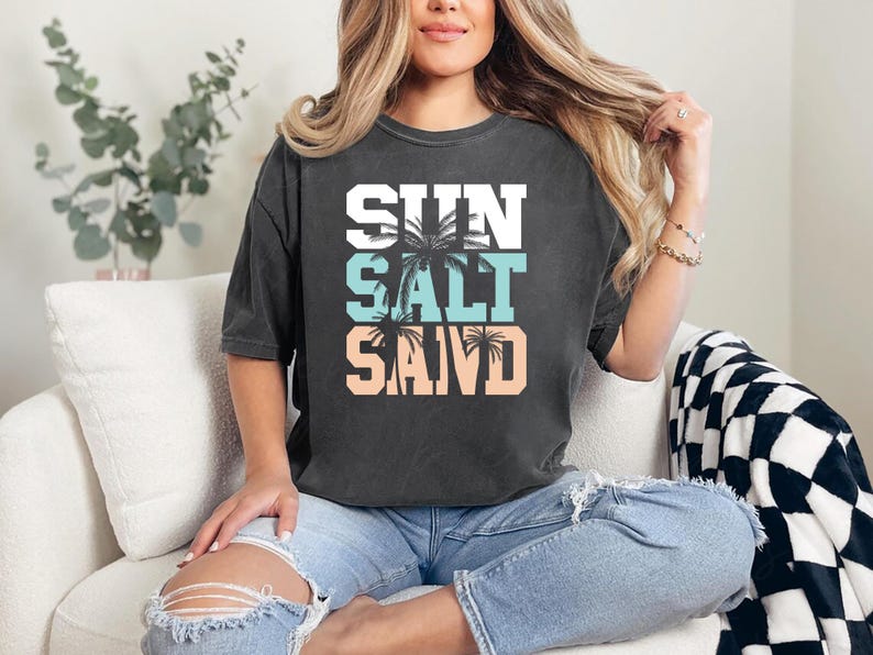 Bold beach-themed graphic with the words 'Sun Salt Sand' in large block letters, featuring palm trees and coastal colors—perfect for summer vacation or beach day t-shirts.