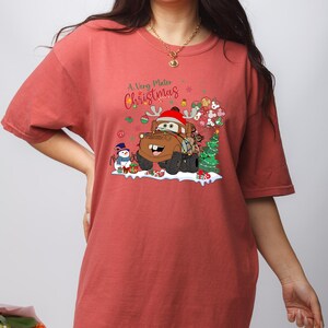 Disney Cars Christmas shirt featuring Mater in a festive holiday scene with lights, snowman, and gifts, perfect for Disney and Cars fans.