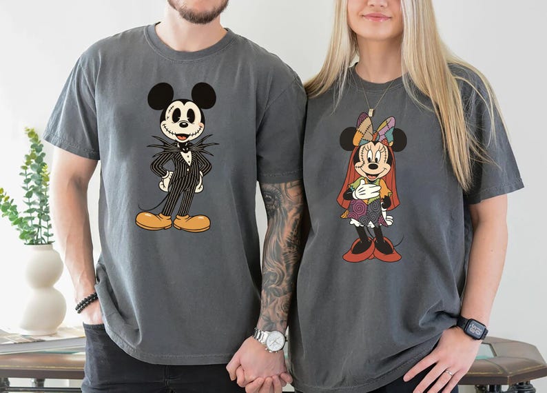 May include: Two gray t-shirts featuring Disney characters. One shirt displays Jack Skellington in a pinstripe suit, the other shows Minnie Mouse in a patchwork dress. Both shirts have short sleeves and a relaxed fit.