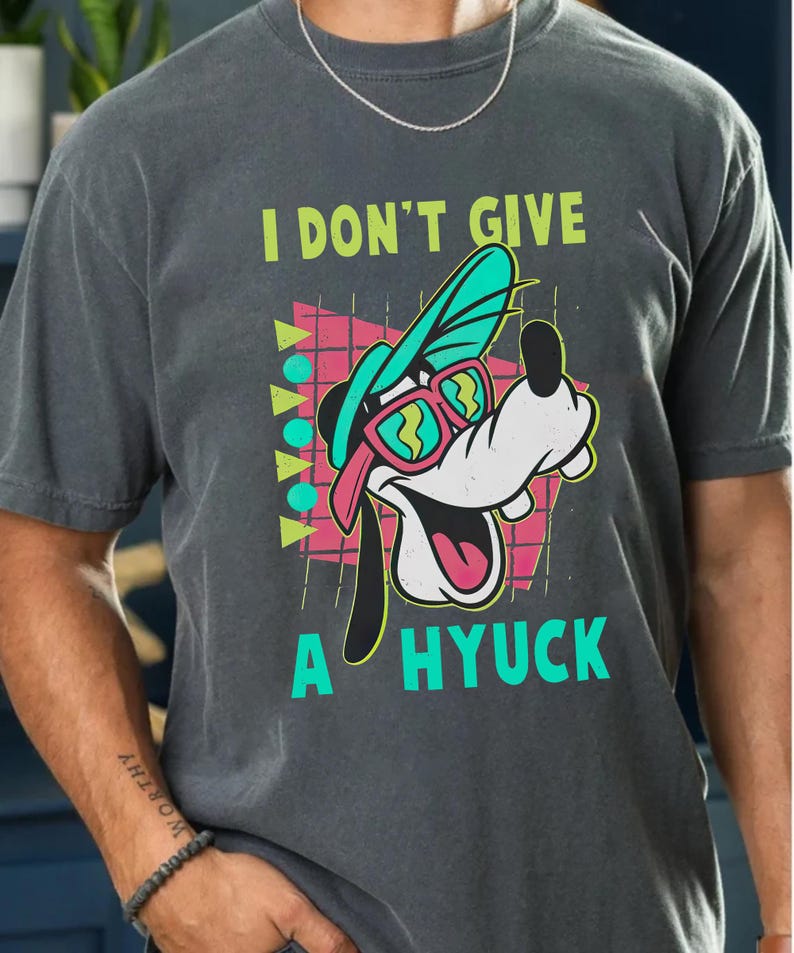 Retro 90s-style Disney shirt featuring Goofy wearing neon sunglasses and a sideways cap with bold text that says "I Don't Give A Hyuck." Colorful geometric background with a distressed vintage look. Perfect for fans of A Goofy Movie, Disney humor shirts, family vacations, or retro-themed Disney park outfits.