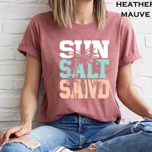Bold beach-themed graphic with the words 'Sun Salt Sand' in large block letters, featuring palm trees and coastal colors—perfect for summer vacation or beach day t-shirts.