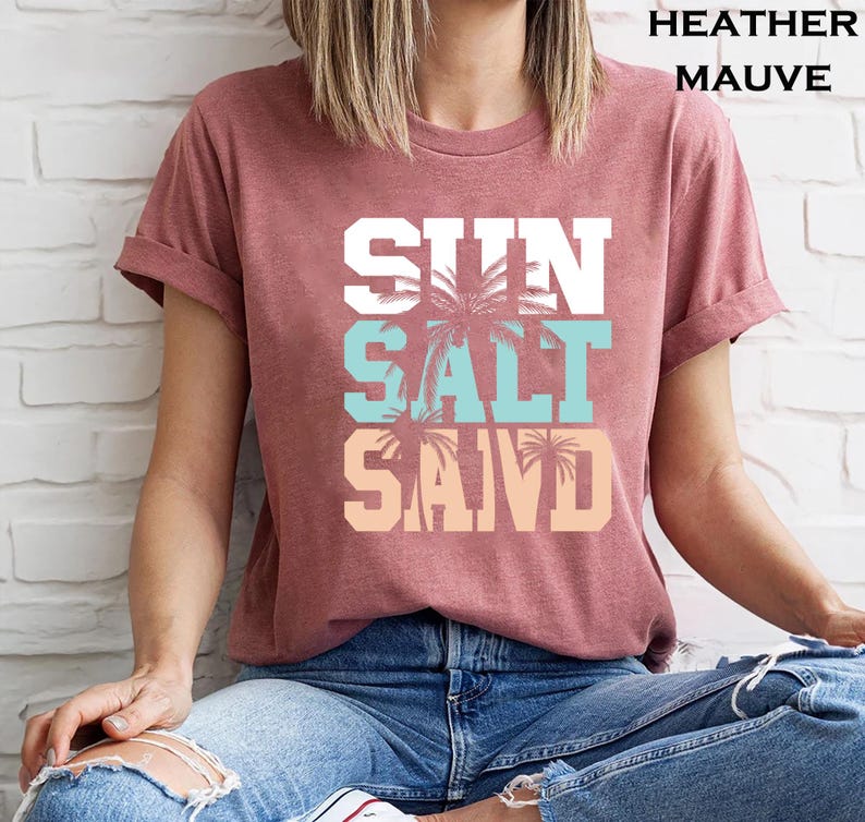 Bold beach-themed graphic with the words 'Sun Salt Sand' in large block letters, featuring palm trees and coastal colors—perfect for summer vacation or beach day t-shirts.