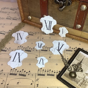 May include: A set of white Roman numeral clock face numbers on a sheet of music. The numbers are in a distressed, vintage style. The numbers are IV, V, VI, VII, VIII, IX, X, XI, and XII. The numbers are arranged in a random order. The sheet music is old and has a brown color. The numbers are on a white background.