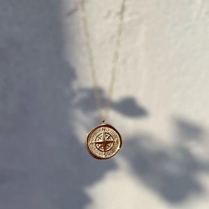 May include: Gold necklace with a compass pendant. The compass is detailed with a star in the center and a circular design around it.