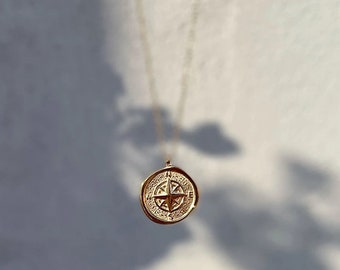 May include: Gold necklace featuring a compass pendant. The compass is detailed with a star in the centre and a circular design around it.