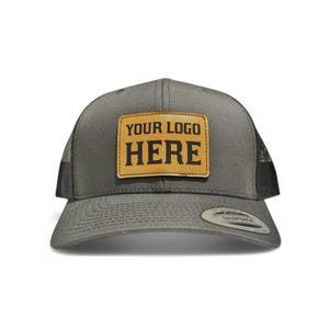 May include: A gray and black trucker hat with a brown leather patch that says "YOUR LOGO HERE" in black lettering.