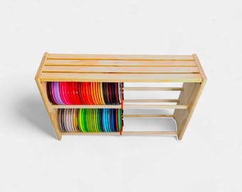 Può includere: Un'unità a scaffale in legno con due ripiani, che contiene un assortimento di dischi di plastica color arcobaleno. I dischi sono impilati ordinatamente sugli scaffali, creando una visualizzazione vibrante.