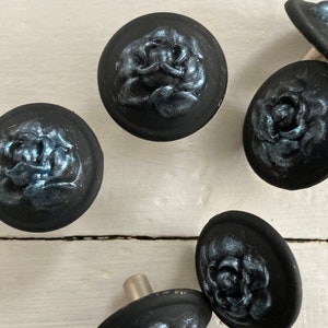 Peut inclure: Cinq boutons de cabinet noirs avec un motif de rose en relief argenté. Les boutons ont une tige en métal argenté.