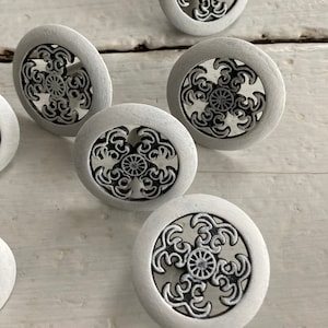 Peut inclure: Six boutons ronds blancs avec un motif noir complexe. Les boutons ont un bord surélevé et un dos plat.