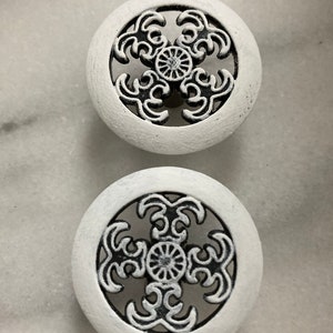 Peut inclure: Deux boutons ronds blancs avec un motif noir complexe. Les boutons ont un centre surélevé et une découpe circulaire au centre.