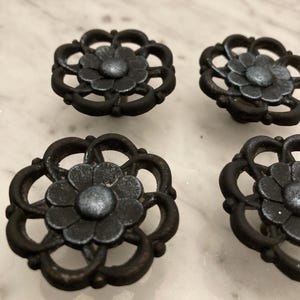 May include: Four black metal drawer pulls with a decorative floral design. The pulls have a distressed finish and a silver centre.