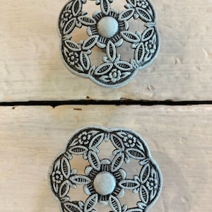 Peut inclure: Deux poignées de tiroir en métal argenté avec un motif floral décoratif. Les poignées sont de forme circulaire avec un centre surélevé et des découpes complexes.