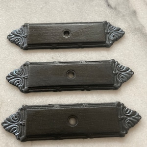 Peut inclure: Trois poignées de tiroir en métal noir avec des détails ornés et un seul trou pour le montage.