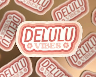 May include: Several pink and white stickers with the text "DELULU VIBES" in a retro font. The stickers have a layered, rounded design with a flower graphic.