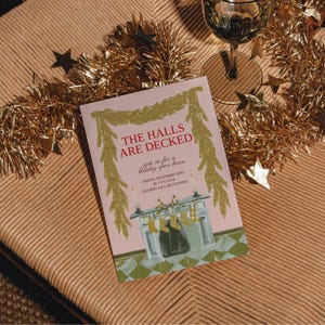 Może przedstawiać: Różowe zaproszenie świąteczne z napisem "THE HALLS ARE DECKED" w kolorze czerwonym. Zaproszenie zawiera ilustrację kominka i złote brokatowe akcenty. Złote girlandy i dekoracje w kształcie gwiazd otaczają zaproszenie, z kieliszkiem wina w tle.