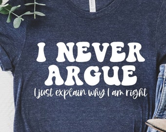May include: A navy blue t-shirt with white text that reads "I never argue I just explain why I am right". The text is in a retro font style. The shirt is laid out on a white surface with a pair of blue jeans and brown ankle boots.