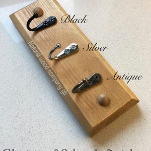 Op de afbeelding: Houten wandhaak met drie metalen haken in zwart, zilver en antiek. De tekst luidt "Choice of 3 hook finishes" en "Natural wood company gb."