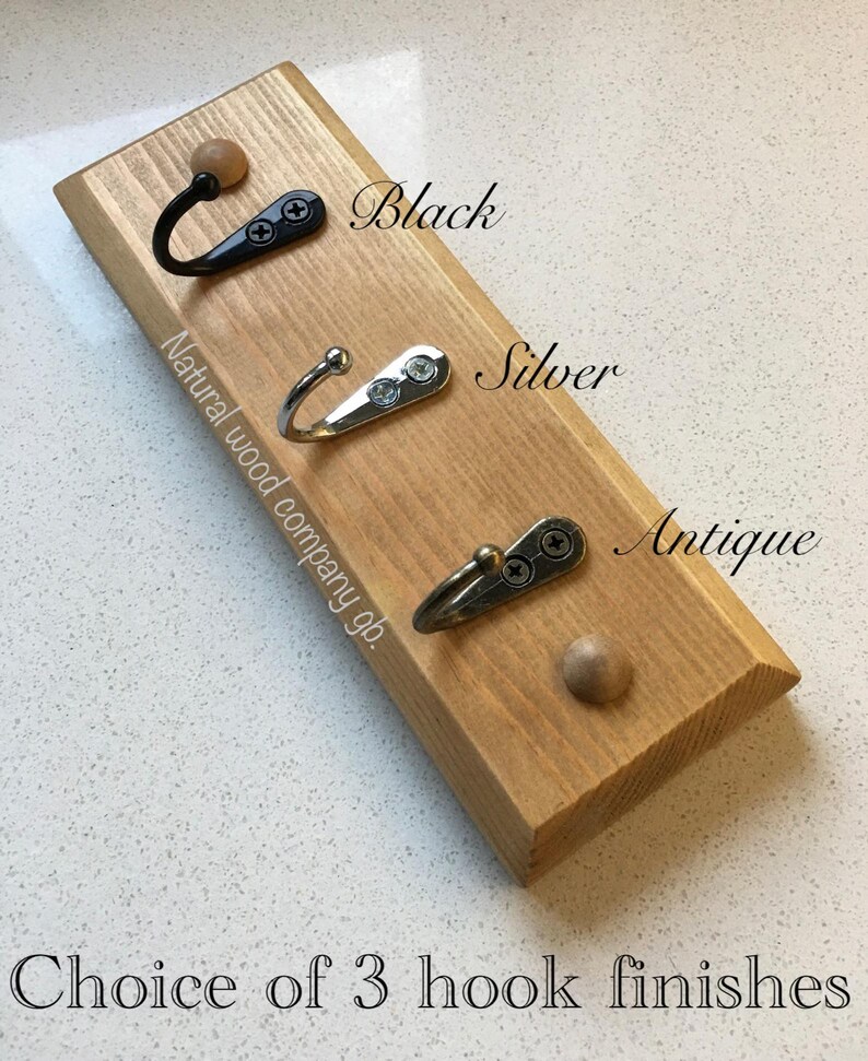 Op de afbeelding: Houten wandhaak met drie metalen haken in zwart, zilver en antiek. De tekst luidt "Choice of 3 hook finishes" en "Natural wood company gb."