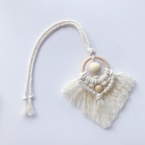 May include: A white macrame wall hanging with wooden beads and a wooden ring. The hanging has a fringe around the bottom.