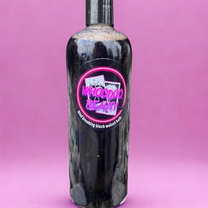 May include: A black bottle of "WHOODOO BEAUTY" bind breaking black walnut bath. The label is a pink neon circle with the brand name and images. The bottle is against a pink background.