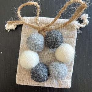 May include: A small, beige drawstring bag with a brown twine closure. The bag contains six felt balls in a mix of white and gray.