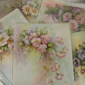 May include: A collection of watercolor floral paintings featuring various blooms in soft pastel colors. The artwork includes daisies, sweet peas, and pansies, with delicate brushstrokes and a vintage aesthetic. The paintings are displayed in protective sleeves.