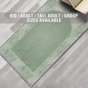May include: A green prayer rug with a white border and a decorative pattern. The rug has a large, rectangular space in the center for kneeling. The text "Saiya" is written in cursive on the rug. The text "KID / ADULT / TALL ADULT / GROUP SIZES AVAILABLE" is written in white letters on a black background at the top of the image.