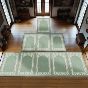 May include: A set of five green prayer rugs with white and gold trim. The rugs are arranged in a staircase pattern, with the smallest rug at the top and the largest rug at the bottom.